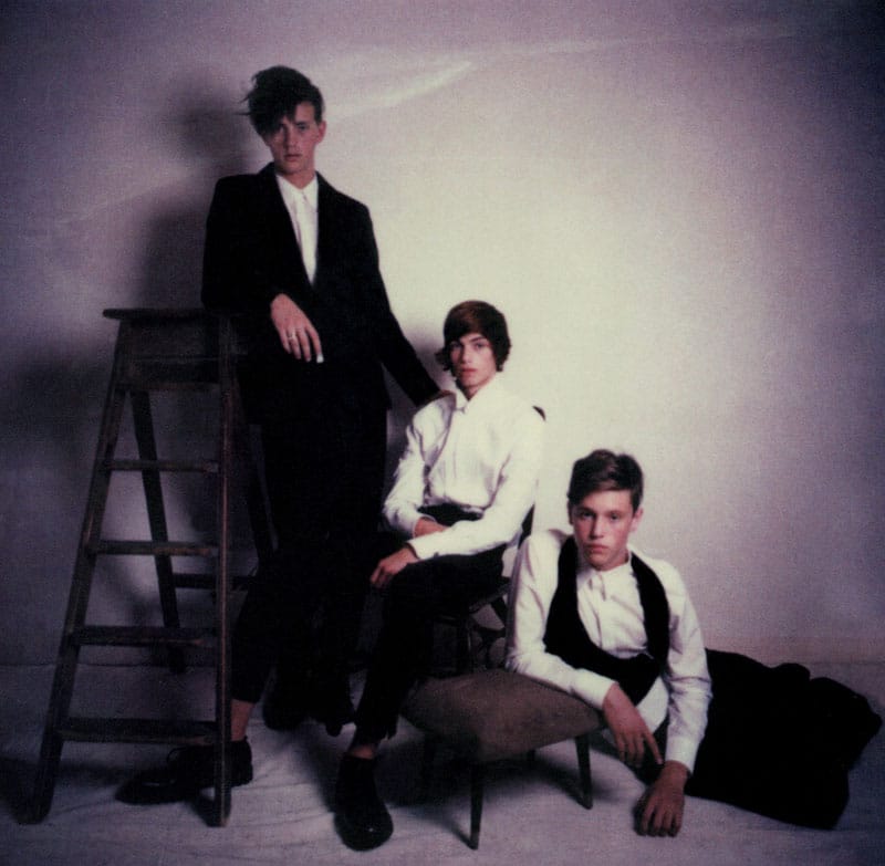 Three stylish young men pose elegantly with dramatic lighting.