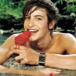 Young man enjoying a red popsicle in a lush, tropical setting.