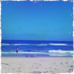 Person walking on Virginia Beach with waves and surfboard.