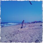 Person practicing paddleboarding on a sunny beach with waves.