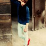 Model in casual blue sweater, mint pants, red shoes, and black scarf.