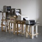 Art installation of stacked printers on wooden stands.