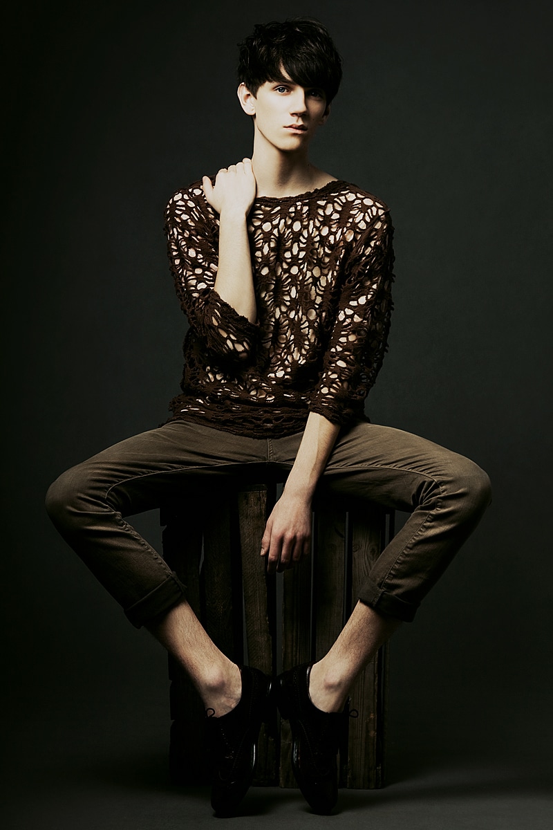 Model in knitted brown top poses on wooden crate.